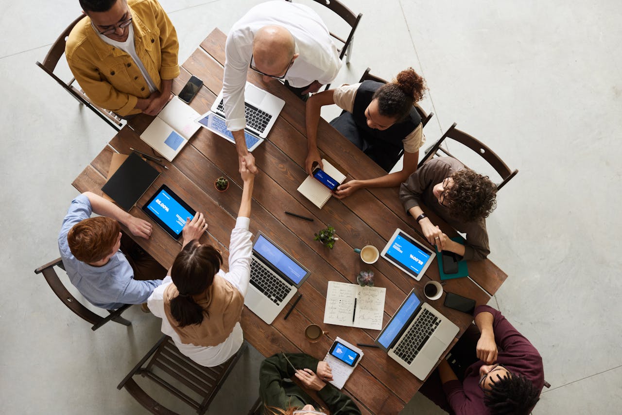 about-01 Top view of a diverse team collaborating in an office setting with laptops and tablets, promoting cooperation.