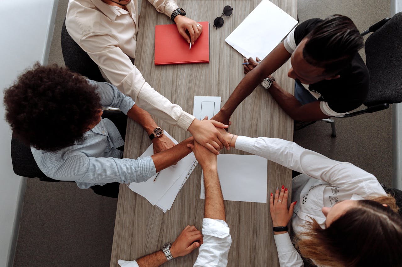services-01 Overhead view of a diverse team placing hands together in a sign of unity during a meeting.